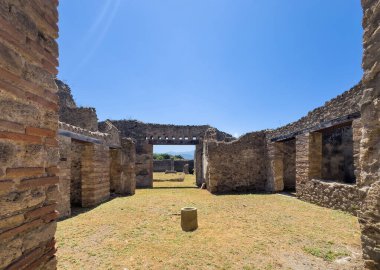 Pompeii, Campania, İtalya - 6 Temmuz 2024: Antik Roma şehri kalıntıları. Vicolo del Balcone Pansile 'in güney tarafındaki mülkte çimenler, silindir taşlar ve mavi gökyüzünün altındaki çimenler görünüyor.