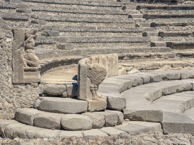 Pompeii, Campania, İtalya - 6 Temmuz 2024: Antik Roma şehri kalıntıları. Piccolo Tiyatrosu ya da sahne arkasından görülen ve oturma sırasının sonundaki iki hasarlı taş heykel üzerine odaklanan küçük tiyatro.