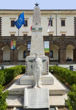 Trevignano Romano, Lazio, İtalya - 7 Temmuz 2024: Monumento ai Caduti, savaş anıtı beyaz mermer asker heykeli ve dikilitaş, Piazza Vittorio Emanuele III, ana meydan. Bitkiler ve Avrupa bayrağı