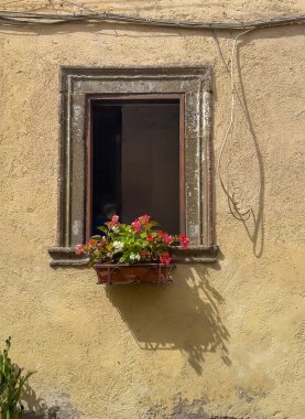 Trevignano Romano, Lazio, İtalya - 7 Temmuz 2024 Via Umberto. Bej cephede, pencerenin hemen dışında duran kapta asılı kırmızı ve beyaz çiçekler. - Yakın çekim. Elektrik kablolarını zar zor tamir ettim.