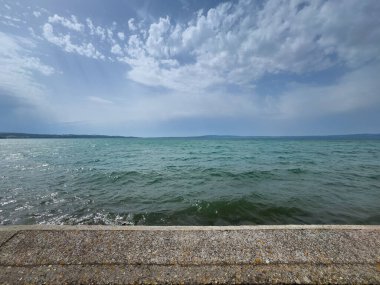 Trevignano Romano, Lazio, İtalya - 7 Temmuz 2024 Bracciano Gölü tarihi şehir merkezinin SE tarafından görüldü. Gök mavisi su ve mavi bulut
