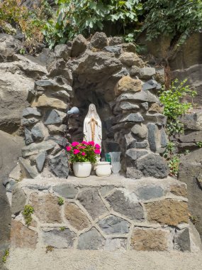 Trevignano Romano, Lazio, İtalya - 7 Temmuz 2024: Mağarada Bakire Meryem heykeli ve Via Guiseppe Garibaldi 'nin güney ucunda bir kap pembe çiçek