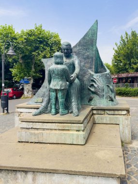 Trevignano Romano, Lazio, İtalya - 7 Temmuz 2024: Piazza Vittorio Emanuele III 'teki bronz heykel Abate Tommaso Silvestri. Arabalar ve restoran işleri arkada.