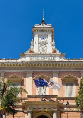Ajaccio, Korsika, Fransa 8 Temmuz 2024: Foch Meydanı 'ndaki Historic Hotel de Ville binası. Mavi gökyüzüne karşı heykelleri olan beyaz saat kulesi. Yeşil palmiye ağacı ve ulusal, Avrupa, şehir bayrakları