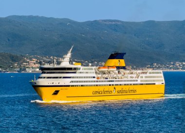 Ajaccio, Korsika, Fransa 8 Temmuz 2024: Korsika Feribotları ve Sardunya Feribotları, aynı gemi, limana girer. Ufuktaki su boyunca orman dağları ve binalarla kıyı şeridi
