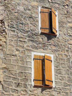 Ocana, Korsika, Fransa - 8 Temmuz 2024: Taşlar ve ahşap panjurlarla kaplı iki pencere arasındaki tipik havan hatlarına sahip tarihi duvar