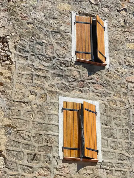 Ocana, Korsika, Fransa - 8 Temmuz 2024: Taşlar ve ahşap panjurlarla kaplı iki pencere arasındaki tipik havan hatlarına sahip tarihi duvar