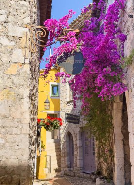 Eze, Fransa - 9 Temmuz 2024: Cuirs and Company Maroquinier, deri işçisi. Aslında, deriden yapılmış lüks ürünler satıyorlar. Sokak boyunca asılı pembe çiçekli tarihi binalar.