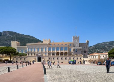 Monako Prensliği, Fransa - 9 Temmuz 2024 Place du Palais, Saray Meydanı. Palais Princier, yürüme yolunun sonundaki sarayda mavi gökyüzünün altında. Dağ arkada. Yayalar hazır.