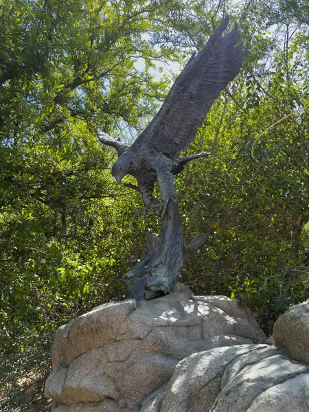 Palm Desert, Kaliforniya, ABD - 26 Nisan 2035 Yaşayan Çöl Hayvanat Bahçesi. Altın Kartal heykeli Ken Bjorge tarafından gri kaya üzerinde ve arkasında yeşil yapraklar