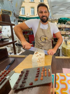 Aix-en-Provence, Fransa - 10 Temmuz 2024: Richelme Meydanı 'ndaki açık pazarda Nougat dükkanı. Satıcının yakın planda dilimlerini kestiği farklı tatlardan oluşan büyük parçalar.