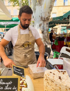 Aix-en-Provence, Fransa - 10 Temmuz 2024: Richelme Meydanı 'ndaki açık pazarda Nougat dükkanı. Satıcının yakın planda dilimlerini kestiği farklı tatlardan oluşan büyük parçalar.