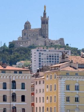 Marsilya, Fransa - 10 Temmuz 2024 şehir merkezi manzarası. Bazilika, Basilique Notre-Dame de la Garde, Muhafız Hanımımız, eski limandan görüldüğü gibi, mavi gökyüzüne karşı tepe üzerinde kuleler