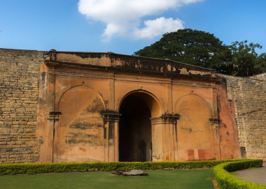 Bengaluru, Tamil Nadu, Hindistan - 4 Ekim 2013: Eski kalenin giriş kapılarından biri. Öğleden sonra güneş ışığı duvarları mavi bulutların altında turuncu renkte. Önde yeşil çimen