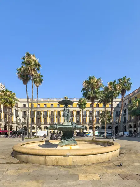 Barselona, İspanya - 11 Temmuz 2024: Barri Gotic, Placa Reial Meydanı. Fuente de las Tres Gracias, Üç Zarafet Çeşmesi, meydanın ortasında. Etraftaki tarihi binalar. Bazı palmiye ağaçları