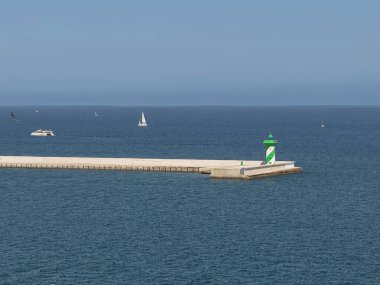 Barselona, İspanya - 11 Temmuz 2024: iskele girişindeki yeşil-beyaz ışık feneri. Mavi sularda bazı eğlence tekneleri