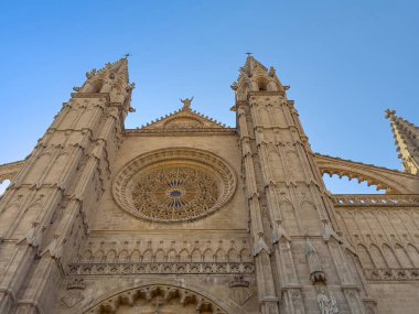 Palma de Mallorca, İspanya - 12 Temmuz 2024: Katedral, Santa Maria de Mallorca. Giriş cephesinin mimarisi kemerin üstünden bakıyor, dev gotik güller, kuleler ve en üstteki Bakire Meryem heykeli.