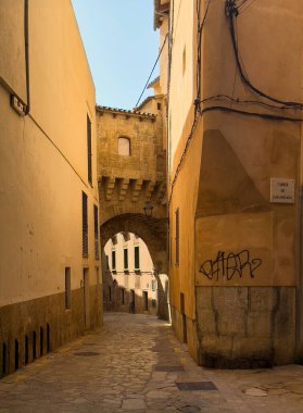 Palma de Mallorca, İspanya - 12 Temmuz 2024: Carrer de l 'Almudaina' ya bakın, tarihi sarı bina duvarları ve üst geçidi olan dar bir sokak, Carrer de Cann Anglada ile bağlantı