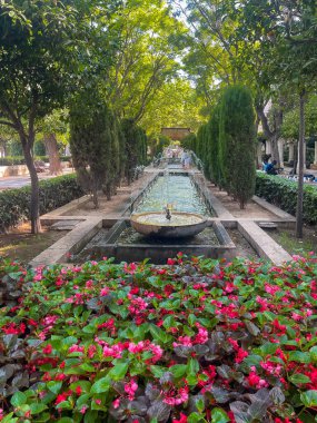 Palma de Mallorca, İspanya - 12 Temmuz 2024: Kralın Bahçesi 'nin orta bölümü, Jardin de tramas, ince fıskiyeli dikdörtgen gölet, önünde kırmızı çiçek, etrafında yeşil ağaç yaprağı