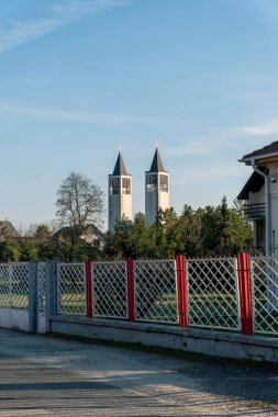 Renkli bir çitin arkasında iki uzun, sivri kule yükseliyor. Yakınlardaki yeşillik, bu sakin yere, mavi gökyüzünün altında huzurlu bir atmosfer ekler..
