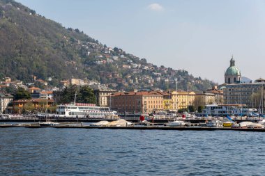 Como, İtalya - 4 Nisan 2025: Como bazilikası (Basilica di San Fedele) ön planda göl manzarası.