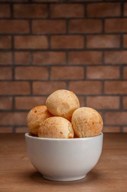 Cheese breads in a white bowl on wooden table and bricks wall background.