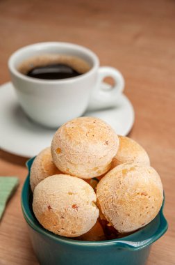 Cheese breads in a green ramekin with a cup of coffee on wooden table.