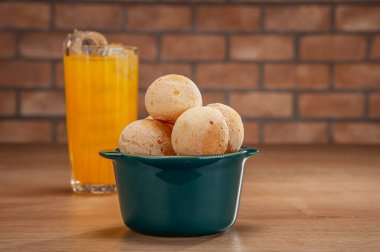 Cheese breads in a green ramekin with a glass of orange juice on wooden table and bricks wall background.