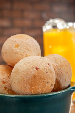 Cheese breads in a green ramekin with a glass of orange juice on wooden table and bricks wall background.