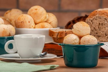 Cheese breads in a green ramekin with a cup of coffee on wooden table and bricks wall background.