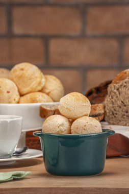 Cheese breads in a green ramekin with a cup of coffee on wooden table and bricks wall background.