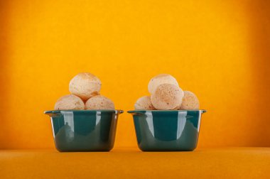 Isolated cheese breads in two green ramekins on orange background.