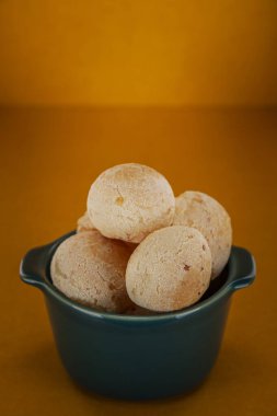 Isolated cheese breads in a green ramekin on orange background.