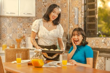 Asian young lady serving cheese bread on breakfast to her sister at the kitchen.