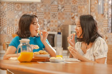 Two young asian ladies having breakfast at the kitchen with oran