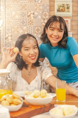 Two asian young ladies having breakfast with brazilian cheese breads and orange juice. (Pao de queijo)