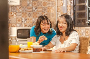 Two asian young ladies having breakfast with brazilian cheese breads and orange juice. (Pao de queijo)