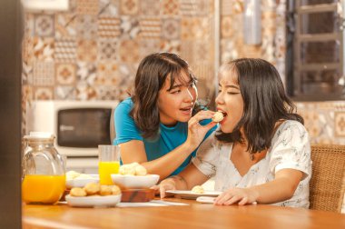 Two asian young ladies having breakfast with brazilian cheese breads and orange juice. (Pao de queijo)