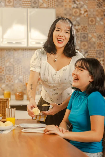 Asian young lady serving cheese bread on breakfast to her sister at the kitchen.