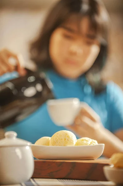 Brazilian cheese breads on the serving dish and a girl putting coffee in a mug.