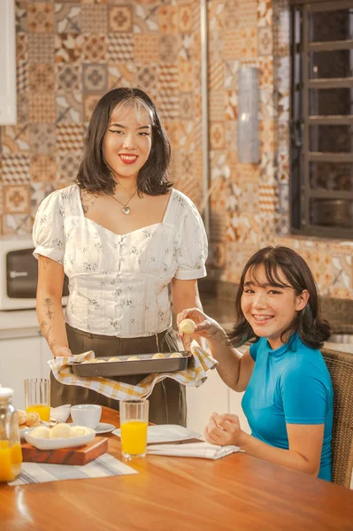Asian young lady serving cheese breads on breakfast to her sister at the kitchen.