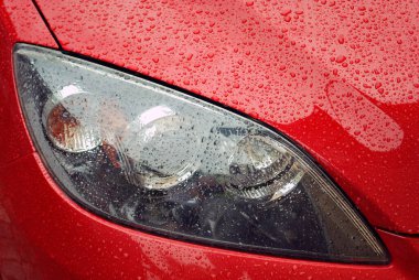 Drops of water after rain on the surface of the red car. Car wet surface. Close-up of the front headlight. Soft selective focus