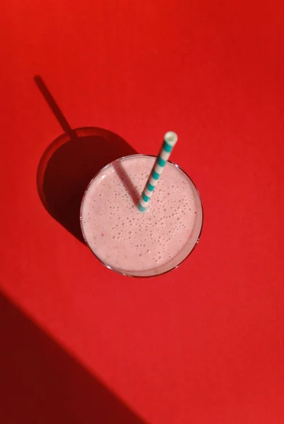 ロングシャドウ トップビューの赤い背景に透明なガラスの中のストロベリーとバナナピンクのスムージー ミルクシェイク 健康的な朝食 — ストック写真