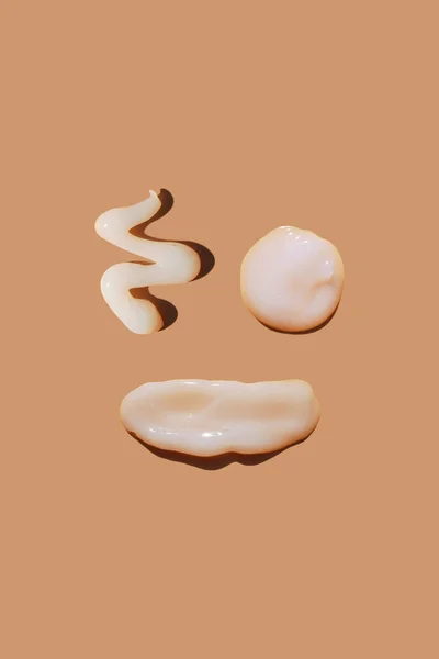 White osmetic smears of creamy texture on a pastel background in the form of a funny face. Concept of face care