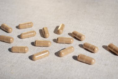 Kahverengi kapsüller bej masa örtüsü arka planına yakın bir yere saçılmış. Beslenme destek kapsülleri. Uzayı kopyala Metin için boşluk