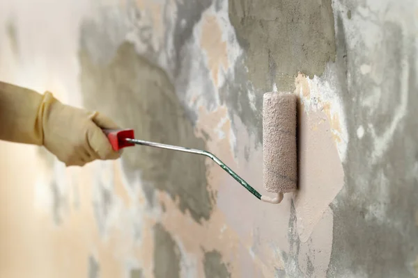 塗装ローラーを使用して家の中で古い壁をペイント手袋で労働者の手の閉鎖 ツールに選択的な焦点 — ストック写真