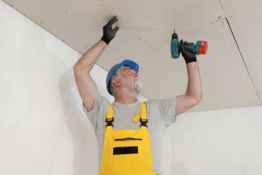 Elektrik güç gişesi tornavidayı kullanarak alçıpan tavanını tamir eden işçiler, enerji verimliliği için mineral yünü yalıtımı üzerine alçı döşeme