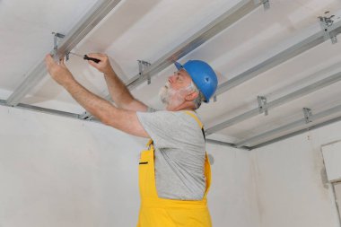 Üst düzey yetişkin işçi alüminyum profil yerleştirerek alçı taşı tavanı ve tornavida kullanarak yalıtım yapıyor