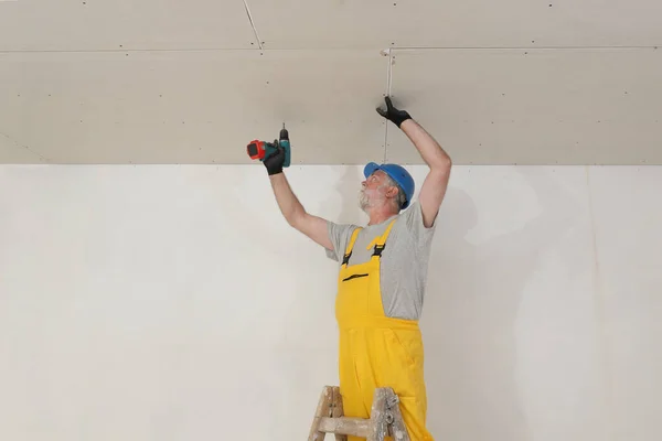 Worker fixing drywall gypsum ceiling using electric power toll screwdriver, plasterboard over mineral wool insulation for energy efficiency