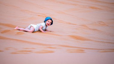 Büyük bir kum tepesinde oynayan iki yaşında bir çocuk..